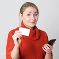 Unsure young blond woman buying on cell phone with credit card Royalty Free Stock Photo