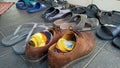 Untidy stack of sandals near brown shoes thrown on the ground.