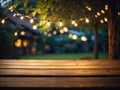 Empty wooden table top with decorative outdoor string lights in the garden at night time