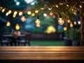 Empty wooden table top with decorative outdoor string lights in the garden at night time