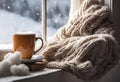 Cozy winter still life: mug of hot tea and warm woolen knitting on vintage windowsill against snow landscape from outside. Royalty Free Stock Photo