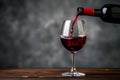 Poring red wine in a glass on the wood table with a gray background
