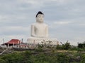 A large, white Buddha statue sits atop a rocky hill, surrounded by greenery. Royalty Free Stock Photo