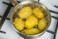 Untreated potatoes boil in a pot on a gas stove.