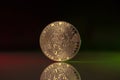 Unus Sed Leo Crypto Coin Placed on reflective surface and lit with green and red lights.