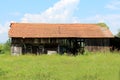 Unused abandoned wooden barn with open space in middle and dilapidated boards surrounded with high uncut grass