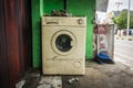 The unused white washing machine with front door near green wall and a broom photo abandoned in a street photo taken in