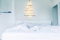 Unusual Christmas tree made of wooden sticks with a garland on the white wall above the bed . Simple, minimal conscientious