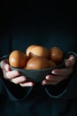 Unusual Easter on dark background. Bowl of brown eggs with hands, vertical