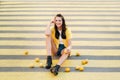 An unusual girl in a yellow shirt, shorts and black shoes with lemons is sitting on a pedestrian crossing in the city. The lemon