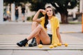 An unusual girl in a yellow shirt, shorts and black shoes with lemons is sitting on a pedestrian crossing in the city. The lemon
