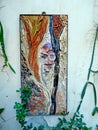 Unusual mosaic panel and green plants on the wall of the house