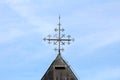 Unusual shiny metal cross on top of old local church roof surrounded with lightning rod and dilapidated metal roof tiles