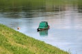 Unusual small wooden river boat with strange closed dark green metal storage cabin anchored next to local grass covered river bank