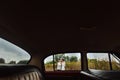 Unusual view of stylish bride and happy groom through red retro car on the background of nature Royalty Free Stock Photo