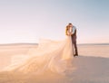 Unusual wedding in the desert. A girl in a white dress ivory shade. Very long plume fluttering in the wind. A loving Royalty Free Stock Photo