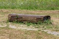 Unusually shaped old public park bench made from narrow wooden boards surrounded with grass and overgrown stone tiles path Royalty Free Stock Photo