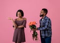 Unwanted confession. Displeased black woman rejecting her admirer with roses on Valentine's Day over pink background Royalty Free Stock Photo