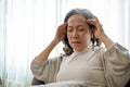 An unwell Asian-aged woman suffers from a headache or migraine while relaxing in living room