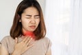 Unwell Asian woman suffering from sore throat, heartburn hand holding her painful neck