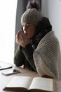 Unwell freeze student in blanket and warm clothes studying while sitting in cold living room. suffer from lack of heat Royalty Free Stock Photo