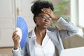 Unwell black business woman hold waver feel sick, hot and overheated work on computer at home office