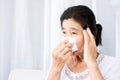 Unwell old Asian woman having flu fever, and headache hand holding paper tissue covering her runny nose and sneezing