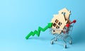 Up arrow and houses in shopping cart on blue background. Market growth in real estate prices