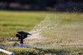 Up close photo of an automatic impact water sprinkler mounted on a custom base of white PVC pipes watering green grass. Royalty Free Stock Photo