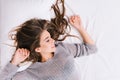 Up portrait cheerful girl with long brunette hair relaxing on white bad. Good morning, positive emotions, smiling with Royalty Free Stock Photo