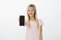 Upbeat girl showing new mobile phone to friends. Happy cute child with blond hair, pulling hand with smartphone