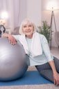 Upbeat senior woman smiling while sitting near yoga ball