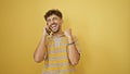 Upbeat young arabian man celebrating his win, confidently talking on smartphone, standing with a big smile against a yellow Royalty Free Stock Photo