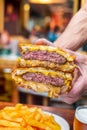 Upclose shot of hands holding a juicy meaty patty melt burger with cheese and grilled onions oozing out of it