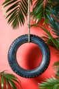 Upcycled Tire Swing Hanging Against Vibrant Red Backdrop with Tropical Palm Leaves Sustainable Outdoor Play Concept