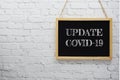 Update Covid-19 typography text on wooden blackboard hanging on white brick wall background Royalty Free Stock Photo