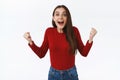 Uplifted and inspired, excited brunette girl in red sweater, clench fists in triumph, having aspirations smiling