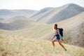 Uplifted young woman going up a slope, surrounded by a beautiful hill scenery.