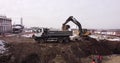 Upper aerial shot: a tractor bucket fills the truck body. An excavator and a truck load the ground. Flight over the