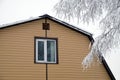 Upper floor with plastic window  in country house wall covered with beige siding and brown metal roof with snow surface and tree b Royalty Free Stock Photo