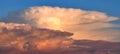 The top of a thundercloud is colorfully lit by the setting sun