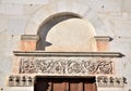 Upper part illuminated by the sun, of the portal carved in low relief, of the basilica of San Frediano in Lucca, with the bell tow