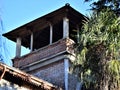 Upper part, immersed in the blue sky, of a tower with small columns and a palm tree in Padua.