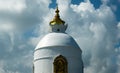 The upper part of the rounded Buddhist Peace Stupa, with a golden spire, against a background of white clouds
