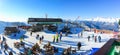 The upper station of the cable car with a rest area and a cafe. People stand or sit at tables. In the background are