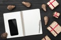 Upper, top view, of Christmas presents on a wooden black rustic background, note pad, pen, phone with space. Royalty Free Stock Photo