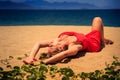 upper view blond girl in red frock lies on sand bends knee