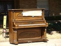 An Upright Piano Sits on a Sidewalk on Trash Day.