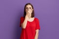 Ups, I said too much. Confused young pretty brunette girl in red t-shirt covering her mouth with palm like she told something bad