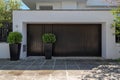 An upscale house entrance with black pedestrian and garage doors and potted plants by the sidewalk. Royalty Free Stock Photo